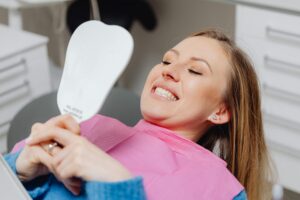 A woman at a dental clinic smiles while holding a mirror, showcasing her dental treatment results.